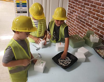 Kids in hardhats practicing hammering pegs into styrofoam