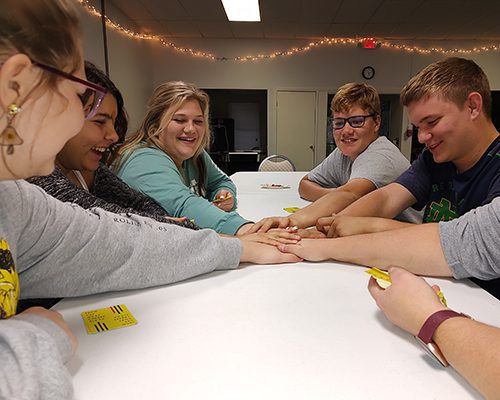 Teens with their hands in the center of a table while playing a game